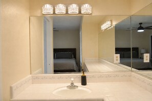 A bathroom with a large mirror, a sink, and a shower area. - Roomy 3BR & 2BA Retreat with Laundry & King Bed (Hanford)
