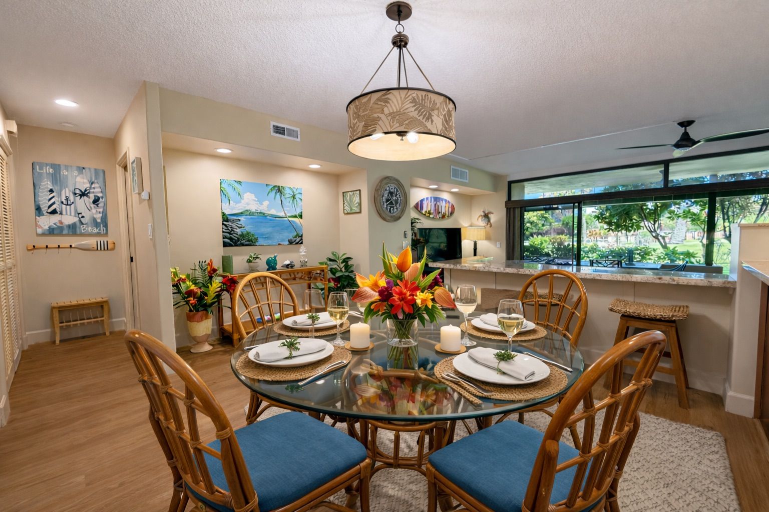 Un espace repas comprenant une table ronde en verre, des chaises en osier et un arrangement floral central.