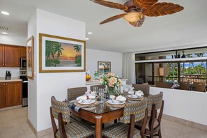 Uma área de refeições com uma mesa de madeira, cadeiras estampadas e um ventilador de teto.