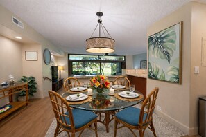 A dining area with a round glass table, wicker chairs, and a hanging light fixture. - Kaanapali Royal 2 Garden View Villas, Sleeps 14 | Car Incl. w/ 6 nights | ML-4013 by KBM (Lahaina)