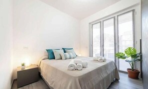 Ein Schlafzimmer mit Bett, Kissen, einem Nachttisch, einer Zimmerpflanze und einem Fenster.