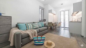 Un apartamento moderno con un sofá gris, un bolso a rayas y un sombrero de paja sobre una alfombra color beige.