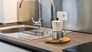 Una cocina con un lavamanos de acero inoxidable, una cafetera y una jarra de vidrio sobre un posavasos de madera.