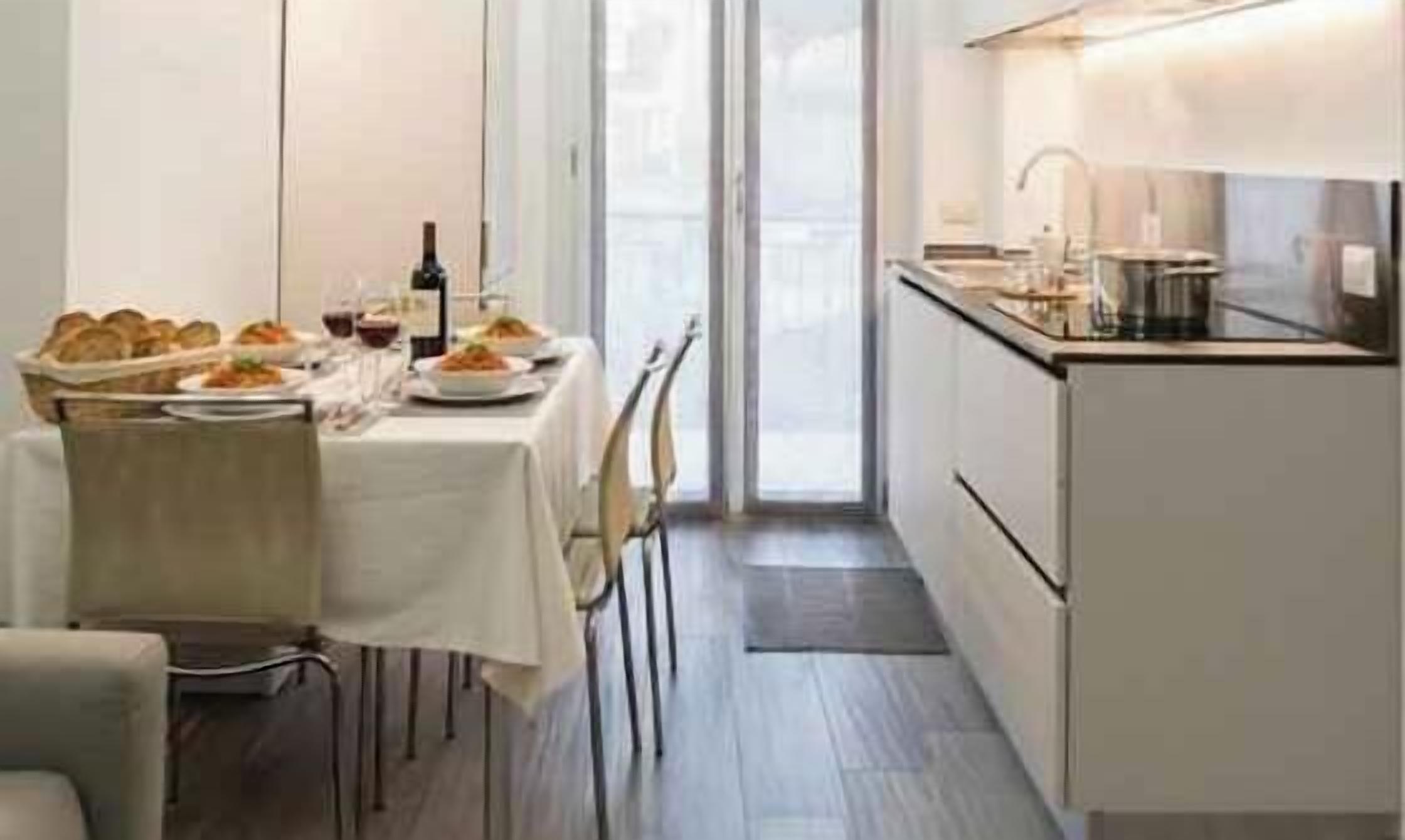 A modern kitchen with a dining table set for two, a wine bottle, and a basket of bread.