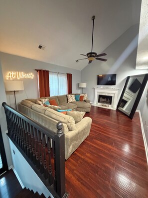 A living room with a sectional sofa, a fireplace, a ceiling fan, and a neon sign. - “Stay Awhile ATL/Modern Retreat Near Airport and Downtown Atlanta (Riverdale)