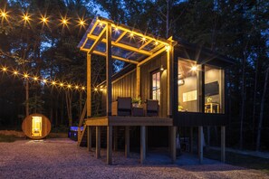 Eine moderne Holz-Hütte mit einer verglasten Terrasse, einer kleinen Sitzgruppe im Freien und einer solarbetriebenen Lampe.