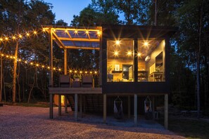 Eine moderne Holz-Blockhütte mit einem gläsernen Essbereich, einer Terrasse mit Sitzgelegenheiten und einer Hängematte.