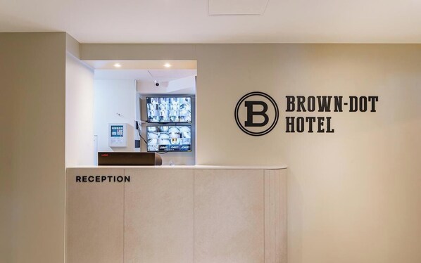 A reception area with a wall-mounted sign for Brown-Dot Hotel, a reception desk, and a security camera.