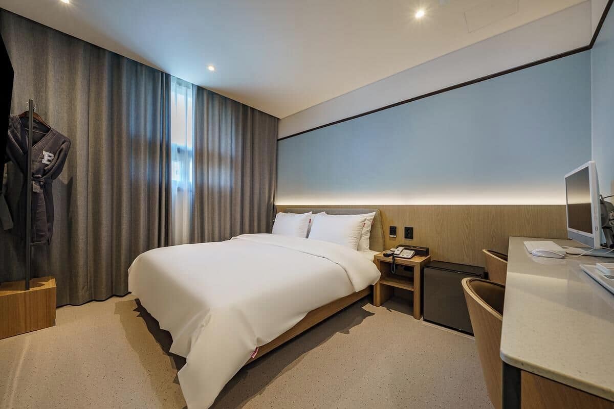 A hotel room with a bed, bedside table, TV, and a desk with a chair.