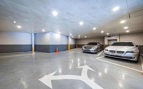 Un garaje de estacionamiento con dos autos, flechas direccionales en el piso e iluminación empotrada en el techo.