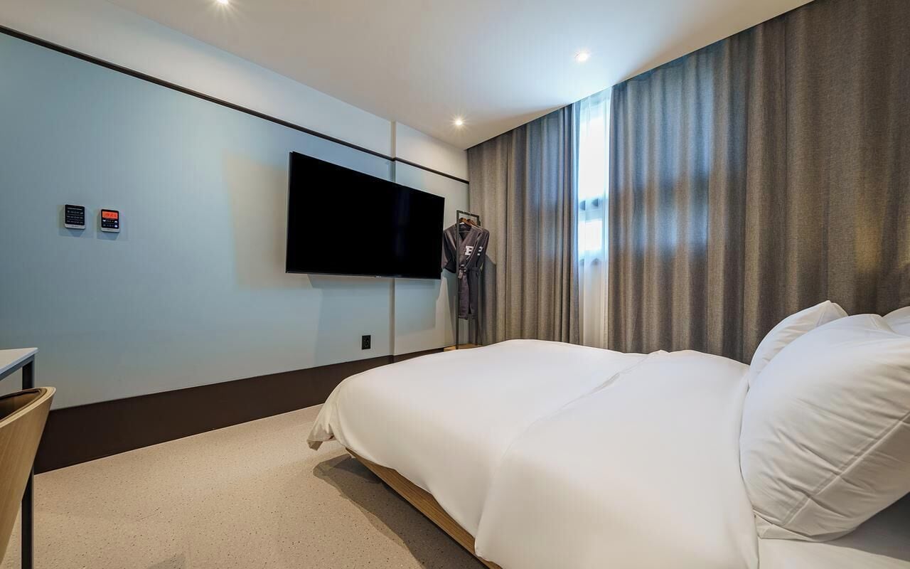Habitación de hotel con una cama grande, un televisor de pantalla plana en la pared, un perchero con bata y una mesita.