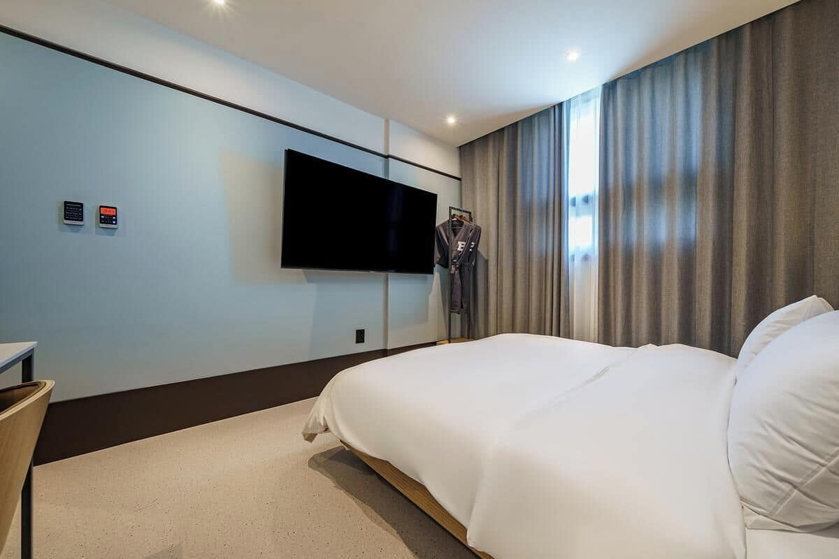 A hotel room with a large bed, a flat-screen TV mounted on the wall, a coat rack with a robe, and a small table.