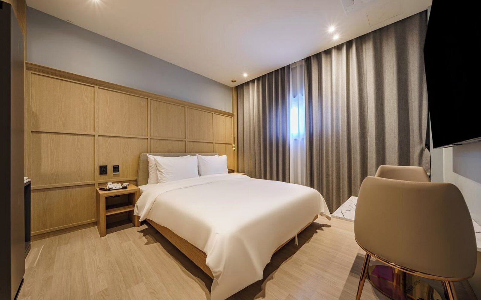 Una habitación de hotel moderna con una cama grande, una mesita de noche, una silla y un televisor.