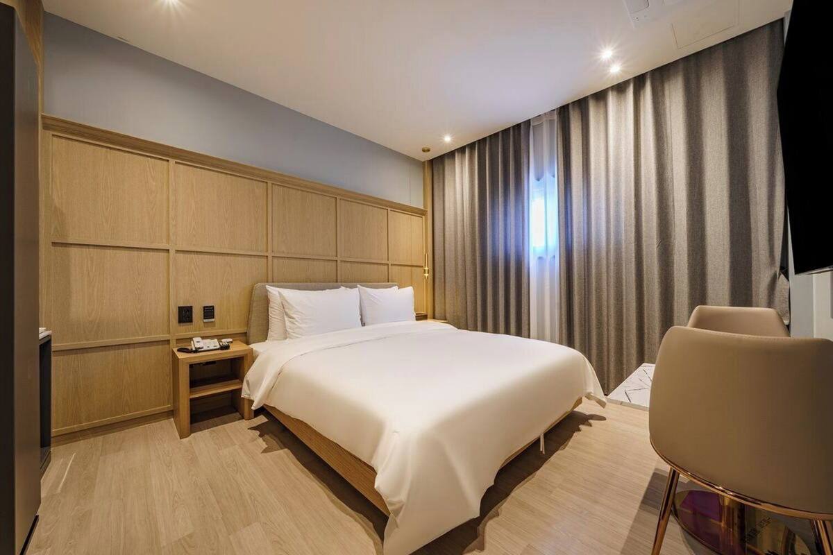 A modern hotel room with a large bed, a bedside table, a chair, and a TV.