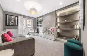 Ein modernes Wohnzimmer mit einem grauen Sofa, Türkis-Armstühlen, einer weißen Raumtrennung und einem Bücherregal.