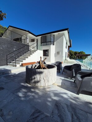 Una casa moderna con un hogar de piedra, asientos al aire libre y una escalera que lleva a un balcón.
