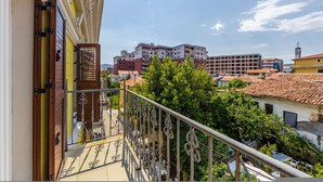 A balcony with a metal railing, a door with a wooden handle, and a view of a multi-story building with red and white facades. - Central G Juhadol 2BR Apartment With Free Parking (Shkodër)