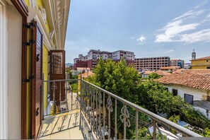 Ein Balkon mit Metallgeländer, eine Tür mit Holzgriff und Blick auf ein mehrgeschossiges Gebäude mit rot-weißen Fassaden.