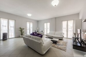 Ein geräumiges Wohnzimmer mit einem weißen Sofa, einem violetten Sessel, einem Couchtisch und einer TV-Konsole.