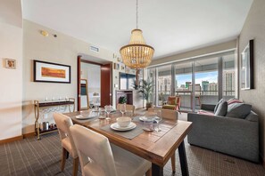 A dining area with a wooden table, chairs, and a chandelier. There is a sofa and a large window with a city view. - Brickell Arch Sea View Balcony Free Parking (Miami)