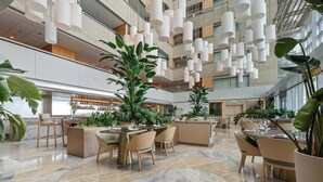 Eine großzügige Hotelhalle mit mehreren Sitzbereichen, einer Bar und hängenden Pendelleuchten.