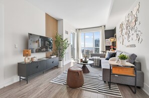 Ein modernes Wohnzimmer mit einem Flachbildfernseher, einem grauen Sofa, einem runden Couchtisch und einem Streifenmuster-Teppich.