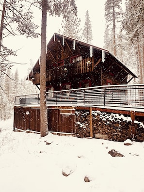 A wooden cabin with a balcony, surrounded by snow-covered trees.
