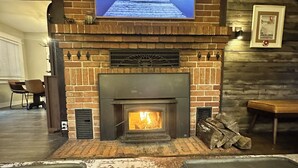 Une cheminée surmontée d’un téléviseur, un banc et une pile de bois de chauffage.