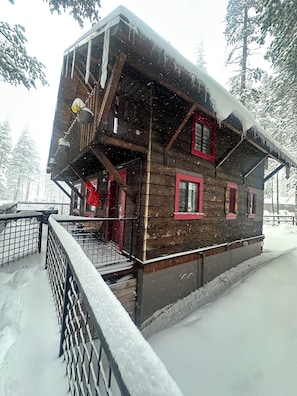 Eine Holzhütte mit Balkon, roten Fensterrahmen und einem mit Schnee bedeckten Dach.
