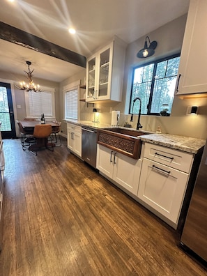 A modern kitchen with white cabinetry, a stainless steel dishwasher, and a dining area with a table and chairs.