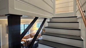 Un escalier avec des marches noires et une rampe en bois, menant à un espace de vie comprenant un canapé en cuir et une lampe.