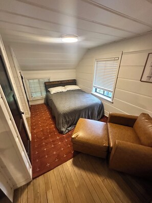 Ein gemütliches Schlafzimmer mit einem Bett, einem braunen Ledersessel, einem Fenster mit Jalousien und einem Deckenventilator.