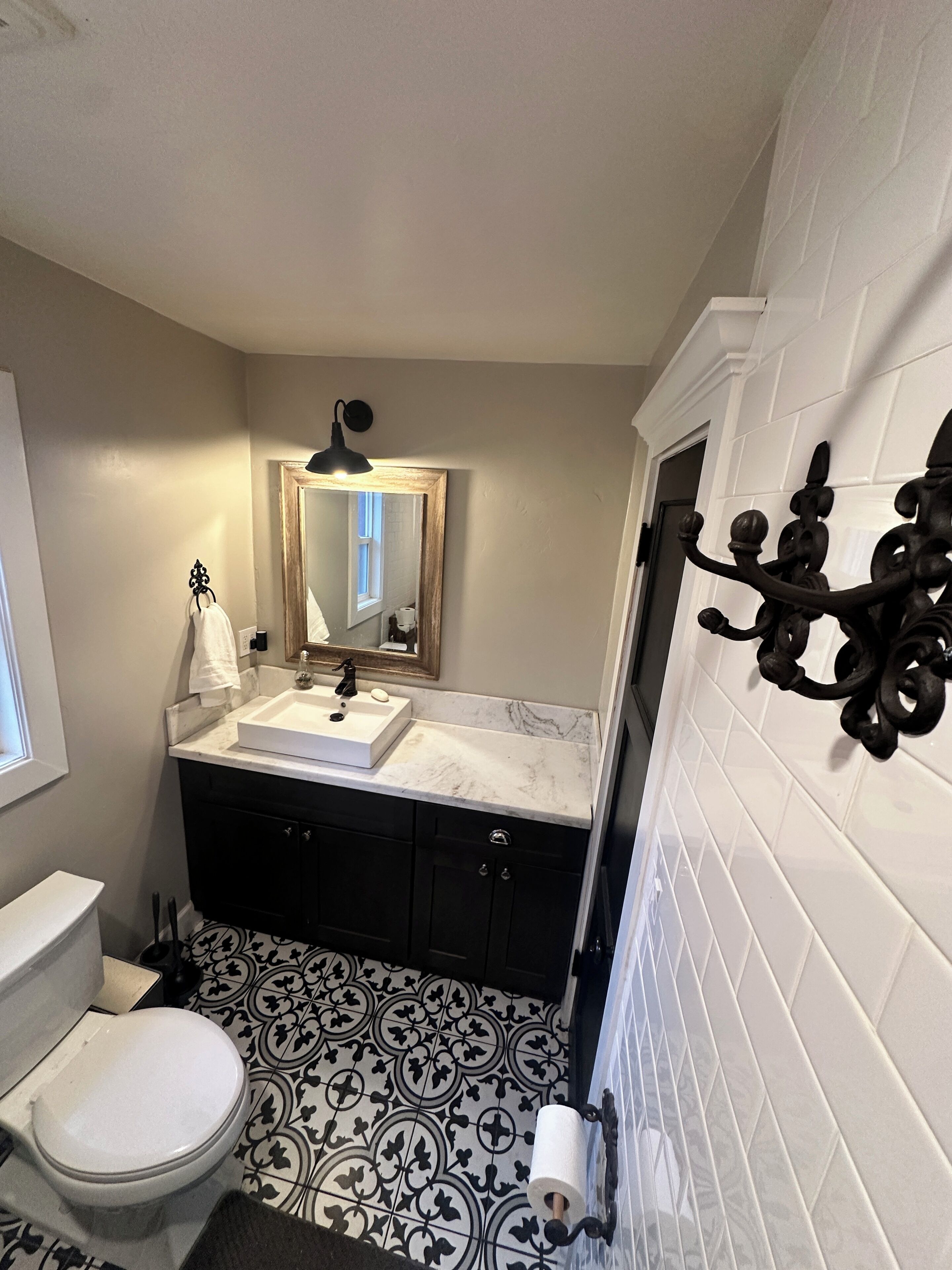 A bathroom with a white toilet, a sink with a mirror above it, black cabinets, and patterned floor tiles.