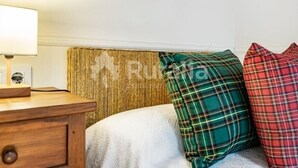A bed with a textured headboard, a bedside table with a lamp, and plaid pillows. - La Casina de Pepa - country house in Roiz, birthplace of Juan de Herrera (Roiz)