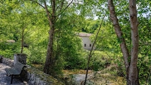 A stone bench by a river with trees and a building in the background. - La Casina de Pepa - country house in Roiz, birthplace of Juan de Herrera (Roiz)