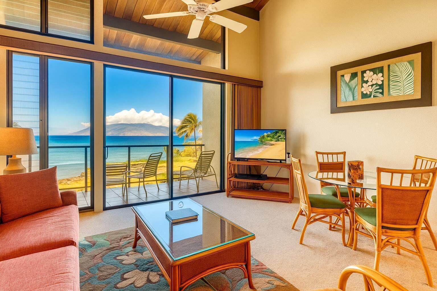 A room with a large sliding glass door, a television, a glass coffee table, wicker chairs, and a red sofa.