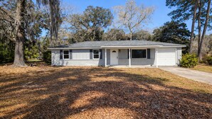A single-story house with a front porch, a garage, and a yard with trees and fallen leaves. - The Vibe House - 3BR Island Retreat near Savannah & Tybee (Savannah)