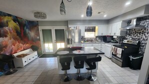 A modern kitchen with a central island, bar stools, a refrigerator, and a microwave. - The Vibe House - 3BR Island Retreat near Savannah & Tybee (Savannah)