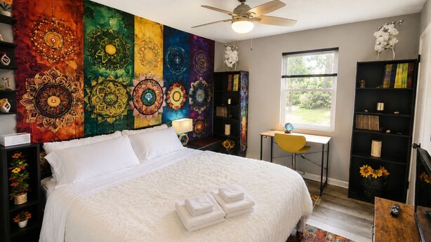 A bedroom with a large bed, a desk, a chair, a bookshelf, and a window. - The Vibe House - 3BR Island Retreat near Savannah & Tybee (Savannah)