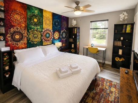 A bedroom with a large bed, a desk, a chair, a bookshelf, and a window.. Charming themed 3-bedroom, 2-bath, Pet Friendly home with Gym, Firepit & Grill