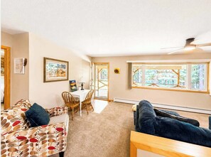 A cozy living room with a sofa, a chair, a table, and a window with a view. - Fenced-in Pet-Friendly Private Wooded Escape (Eagle River)