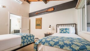 Une chambre avec deux lits, une table de chevet, une lampe, un tableau encadré et une fenêtre.
