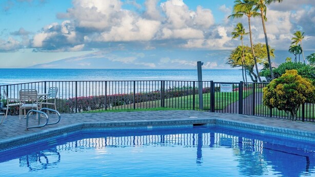 Une piscine avec vue sur l’océan, un espace clos avec des chaises et des palmiers.