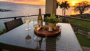 Une table avec deux verres à vin, une bouteille et une plante, sur un balcon donnant sur un coucher de soleil.