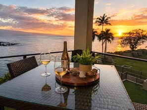 Ein Tisch mit zwei Weingläsern, einer Flasche und einer Pflanze auf einem Balkon mit Blick auf einen Sonnenuntergang.