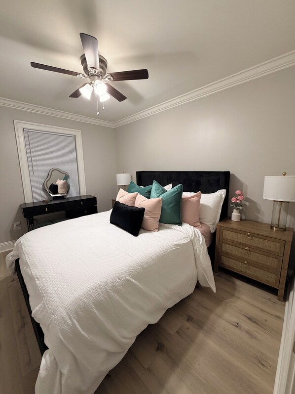 A bedroom with a bed, a nightstand, a dresser, a ceiling fan, and a window with blinds.