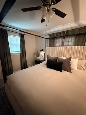 Ein Hotelzimmer mit einem großen Bett, einem Deckenventilator, einem Nachttisch mit Lampe und einem Fenster mit Vorhängen.