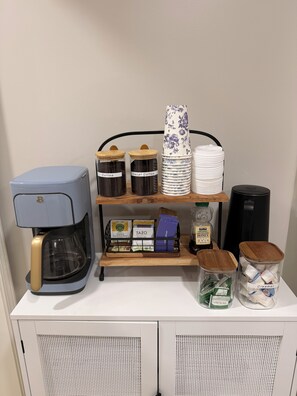 A coffee station with a coffee maker, decaf coffee, creamer, and organic honey.