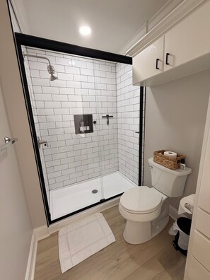 Un baño moderno con ducha acristalada, inodoro blanco y suelo de madera.