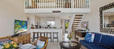 Un vaste espace de vie doté d’un haut plafond, comprenant un coin repas, un canapé, une table basse et une cuisine à l’arrière-plan.